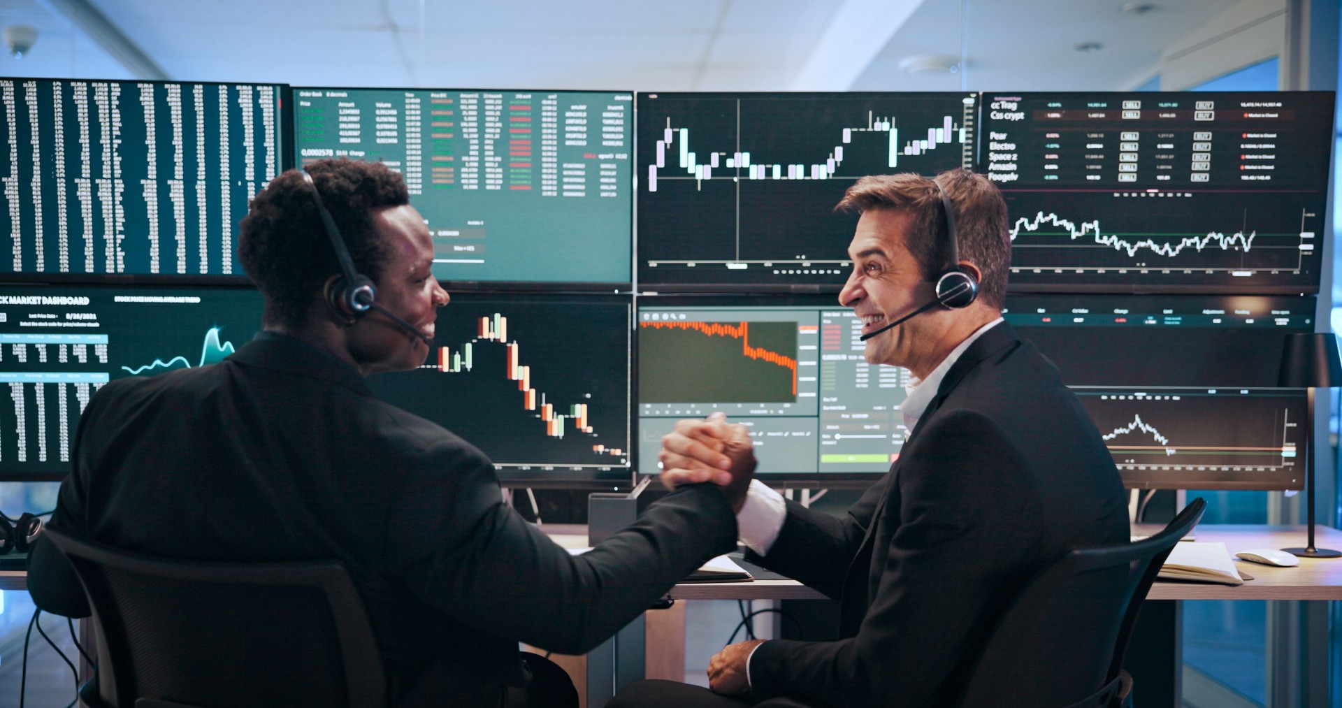 Business people, screen and computer with handshake of trading, partnership and increase of stock market. Men, headset and monitor for graphs, investment charts and profit growth of value achievement